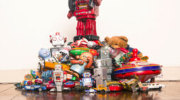 A red robot stands on top of a pile of collectible toys, such as a vintage teddy bear.